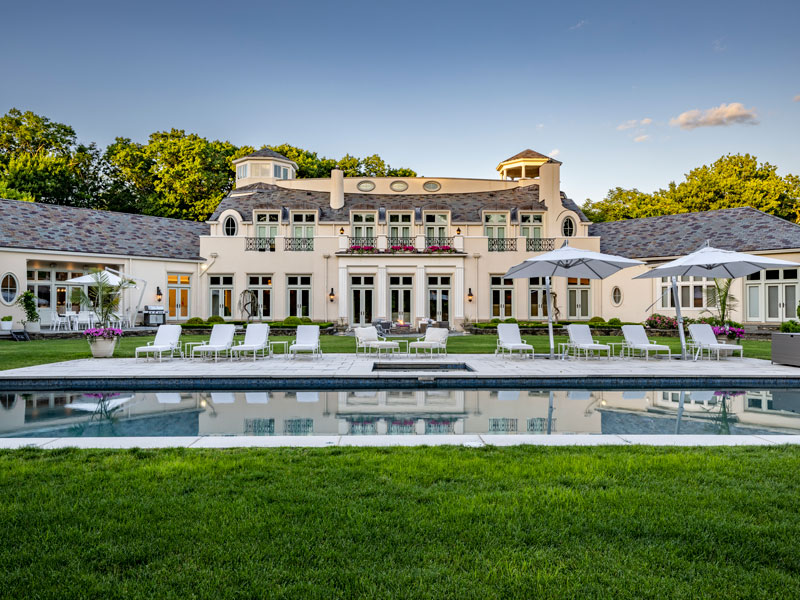 Luxurious mansion with pool and pool lounges in foreground